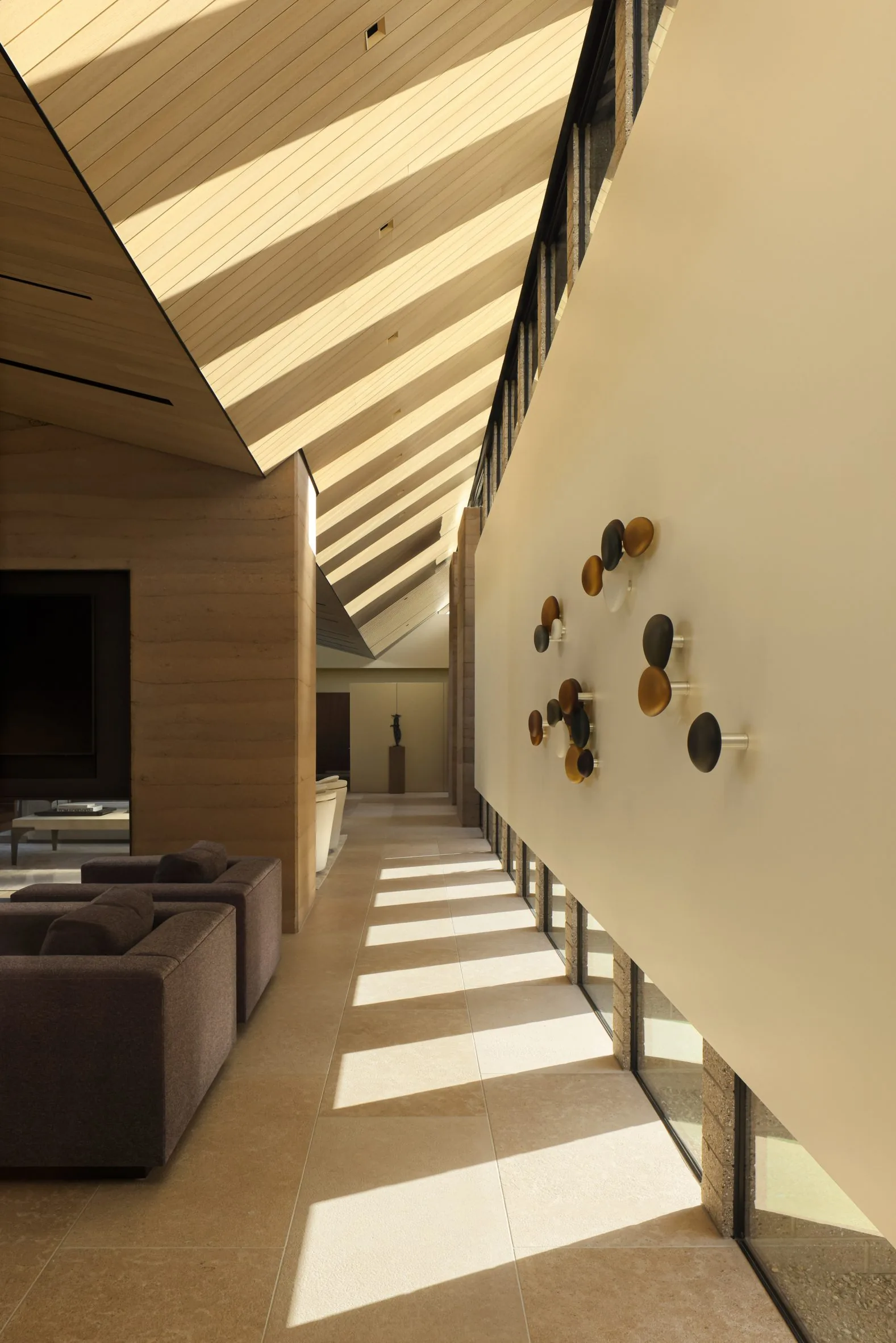 A gallery washed by raking light from a slatted clerestory, art along the wall.