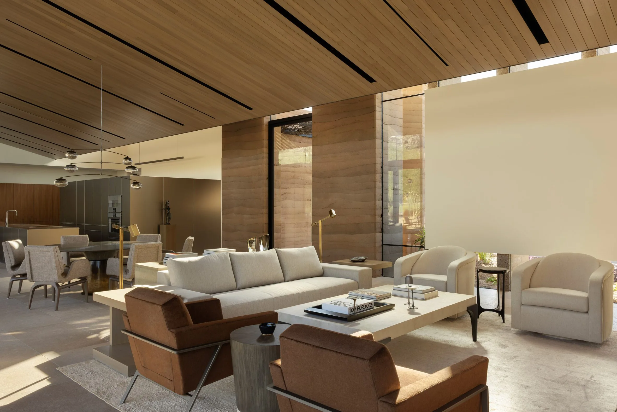 A sun-drenched living room beside a rammed-earth column and full-height glazing.