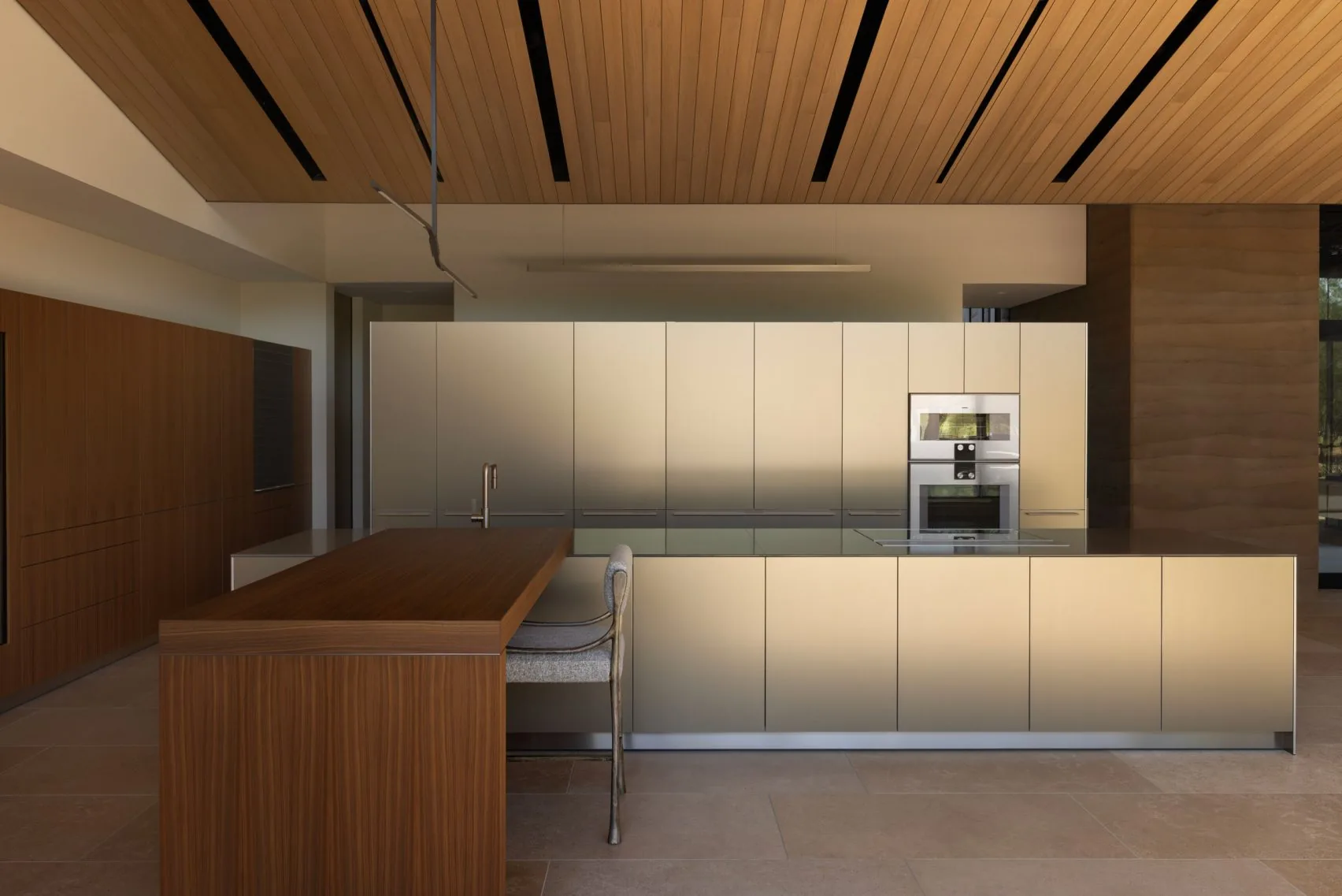 The kitchen with a long timber island under a slatted timber ceiling.