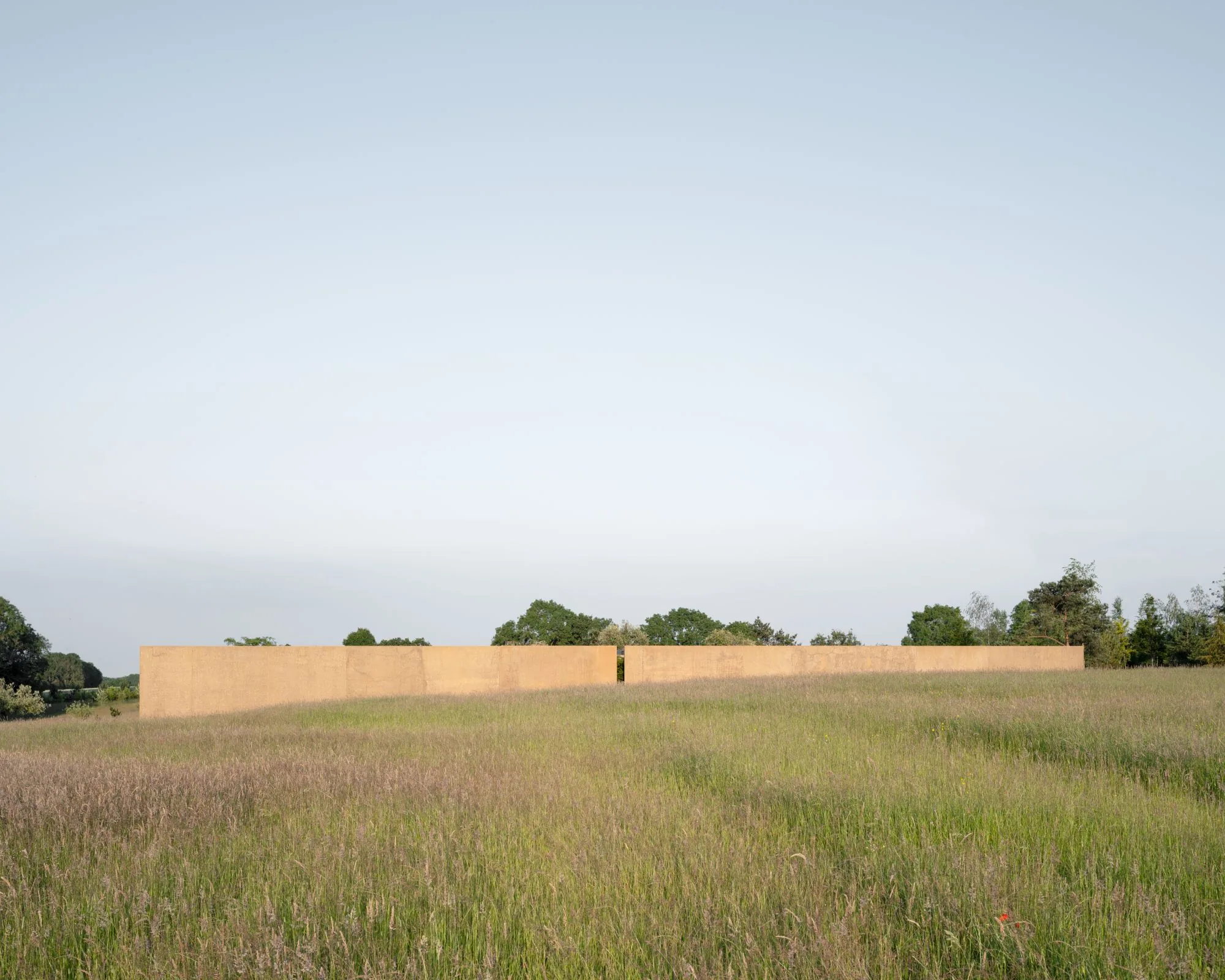 A long rammed-earth wall sitting low in an Oxfordshire meadow.
