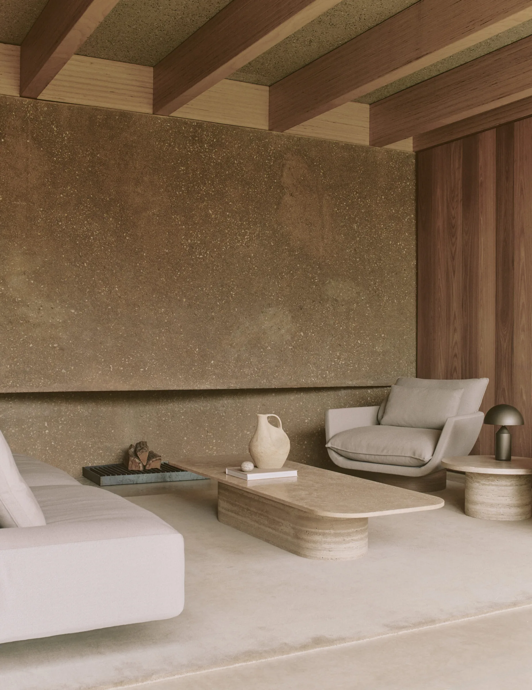 A living room set against a warm rammed-earth wall with a low travertine table.