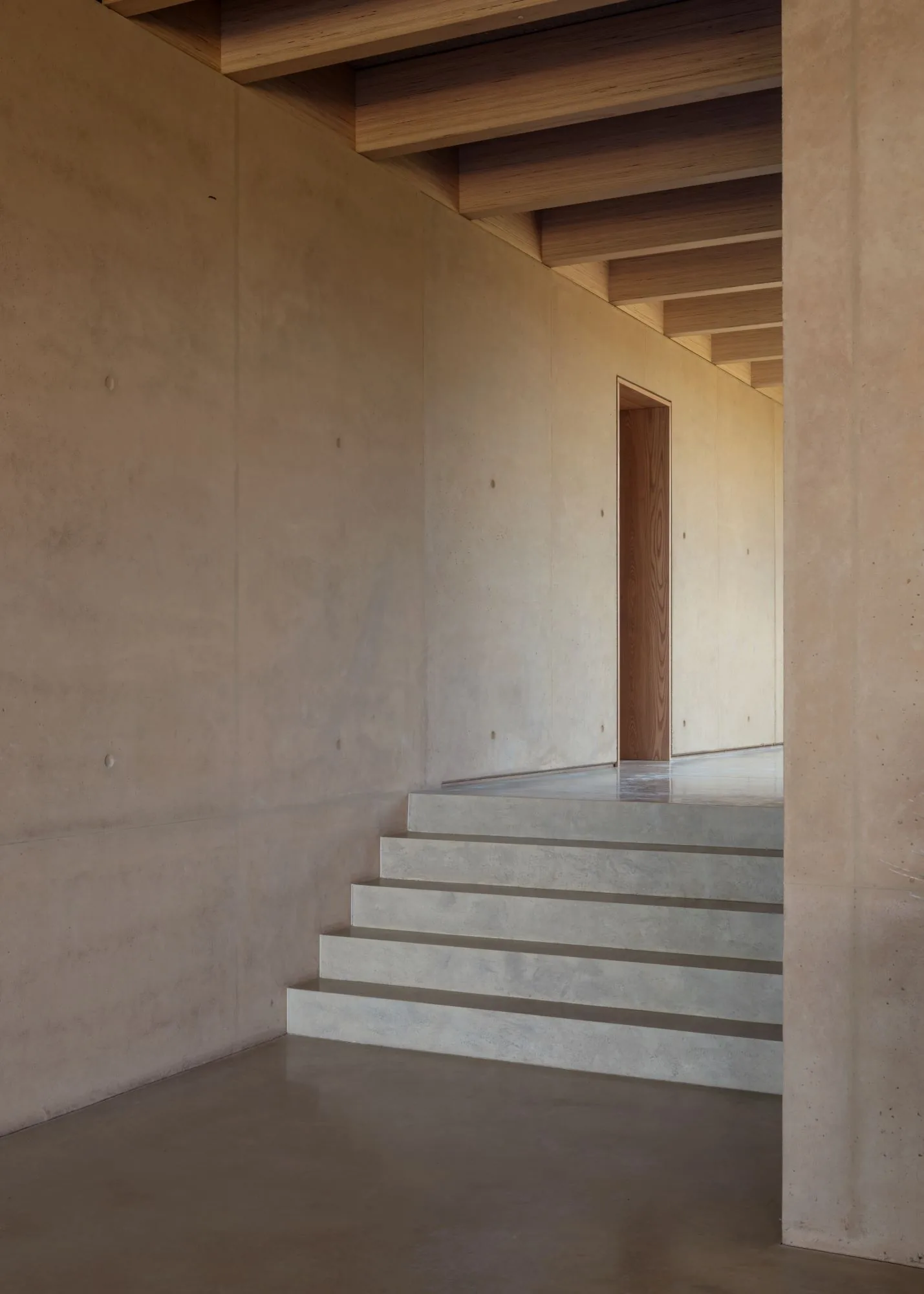 A quiet flight of cast concrete stairs rising between earth-coloured walls.