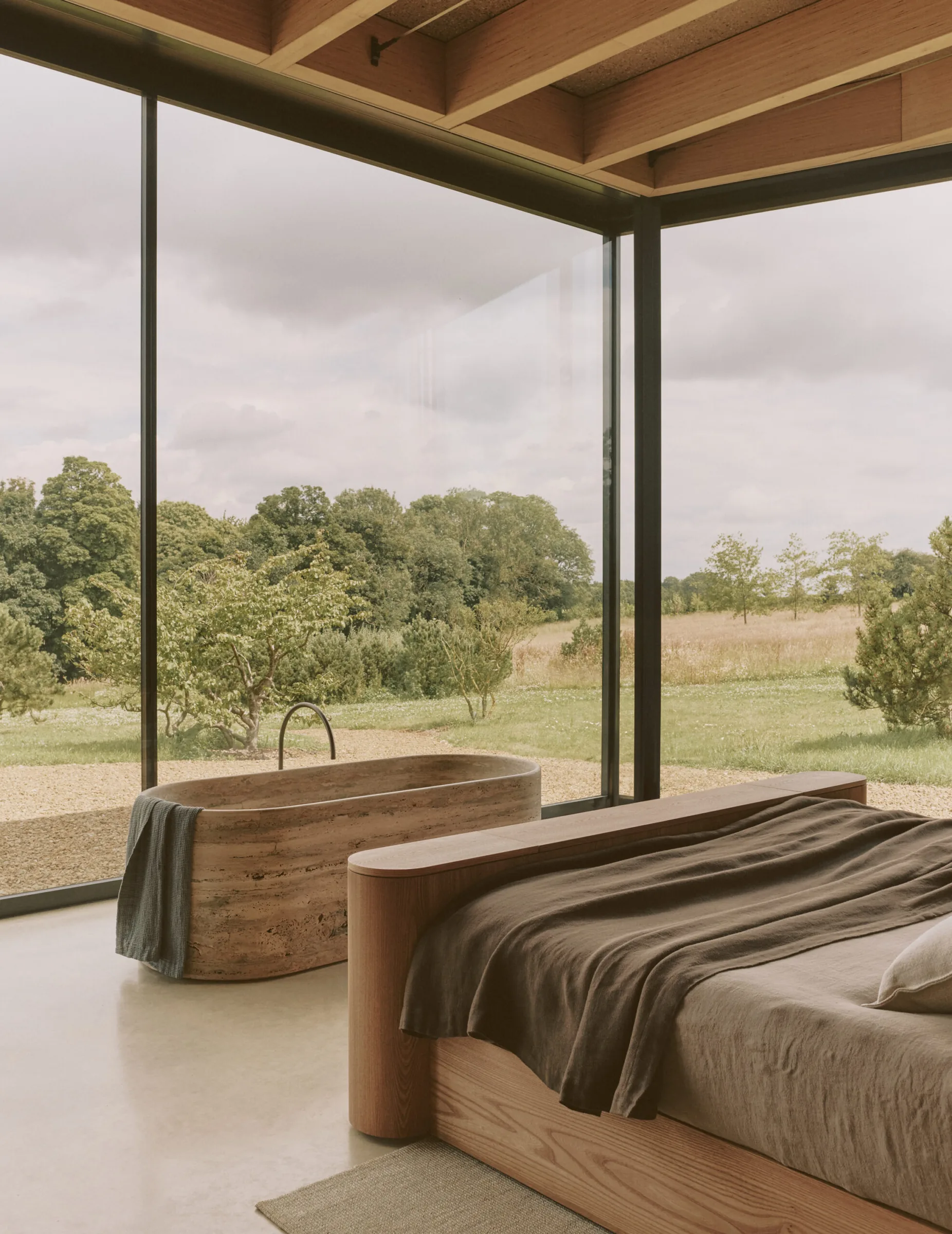 A bedroom with a freestanding stone bath set against full-height glazing.