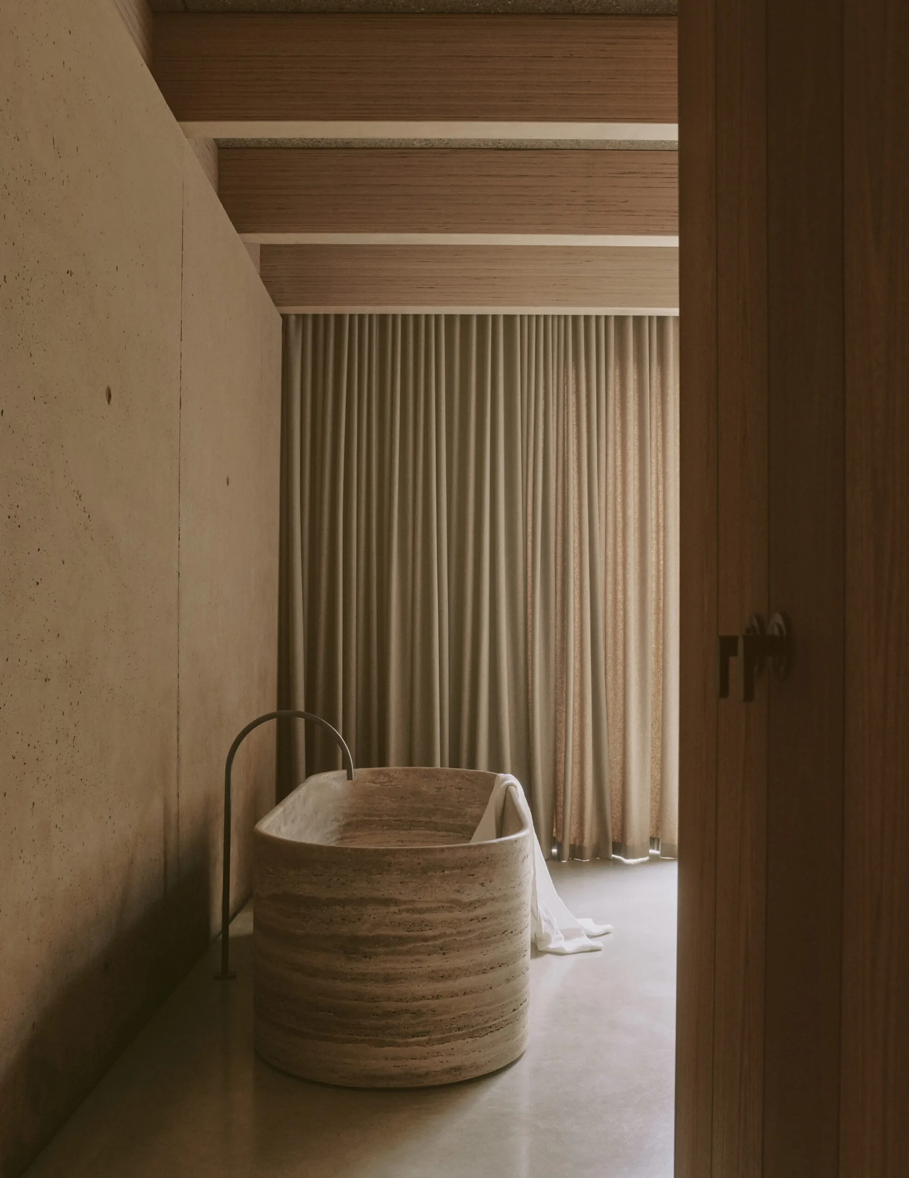 A travertine bath beside a softly curtained window.