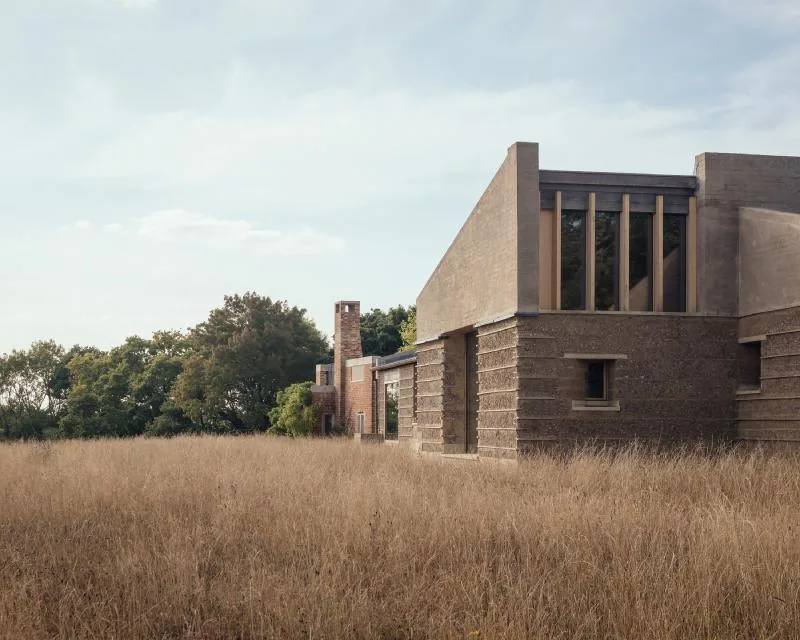 A rammed-earth wall and chimney at Marl House, seen across the long grass.