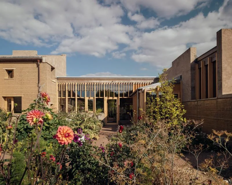 A walled courtyard with planting, between two earth volumes joined by a timber-and-glass link.