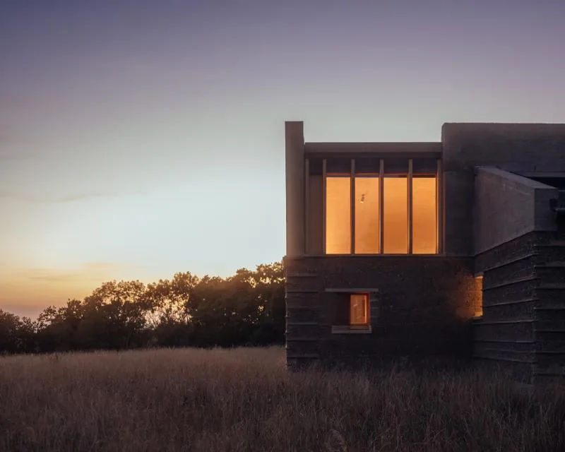 Marl House, rammed-earth volumes glowing at dusk in a Wiltshire meadow.