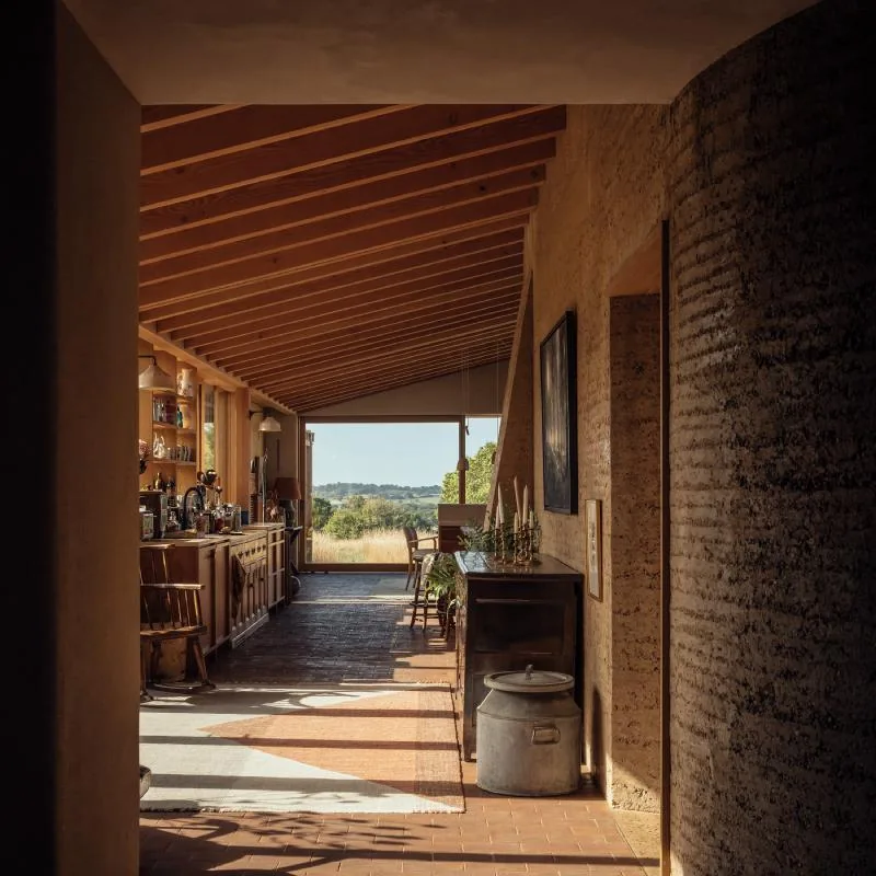 The kitchen gallery beneath an exposed fir roof, beside a curved rammed-earth wall.