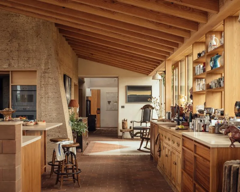 The kitchen running beneath an exposed fir roof, a rammed-earth column at its heart.