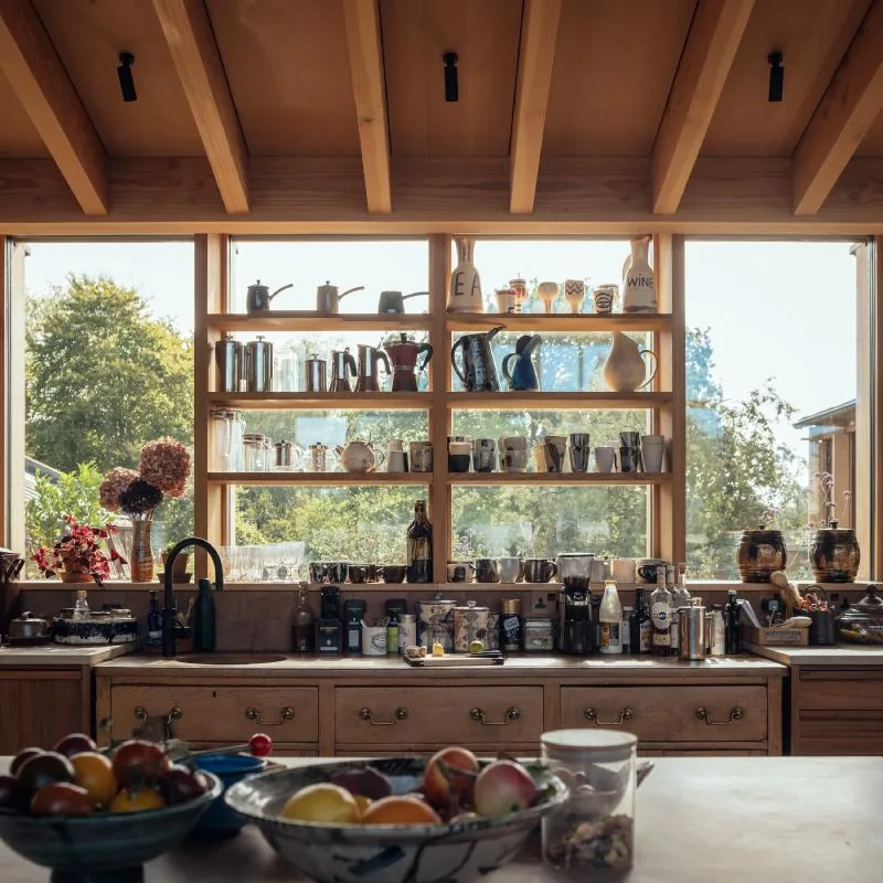 Open shelves of pottery against the kitchen window, the meadow beyond.