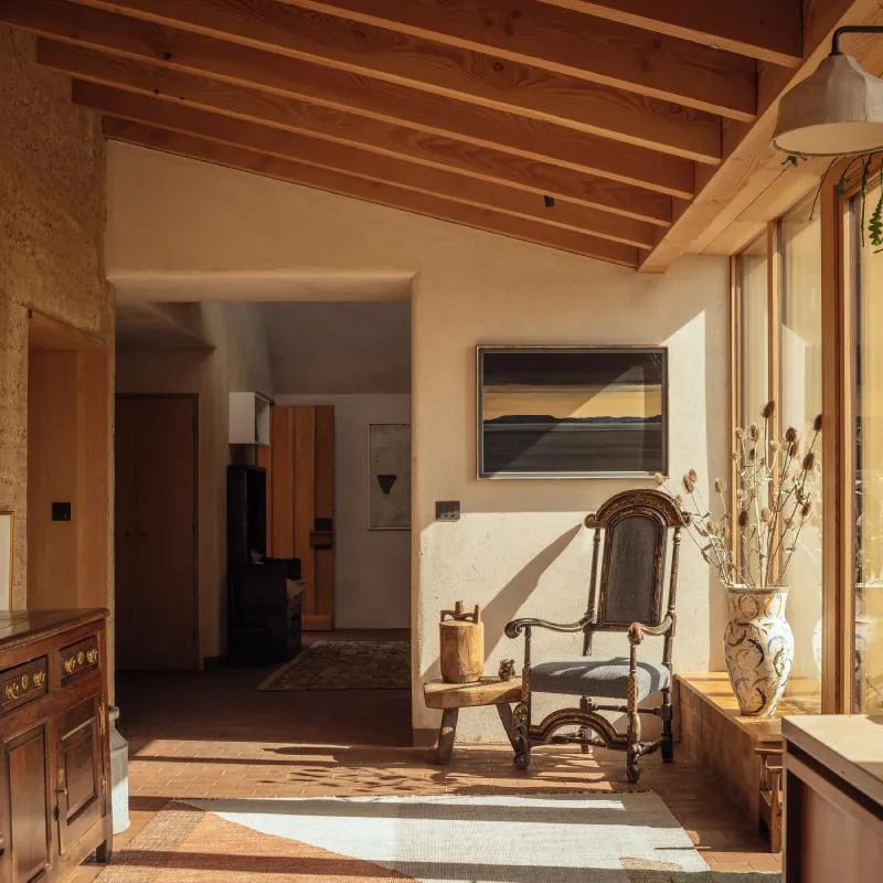 A sunlit living room with exposed beams, plaster walls and an antique chair.