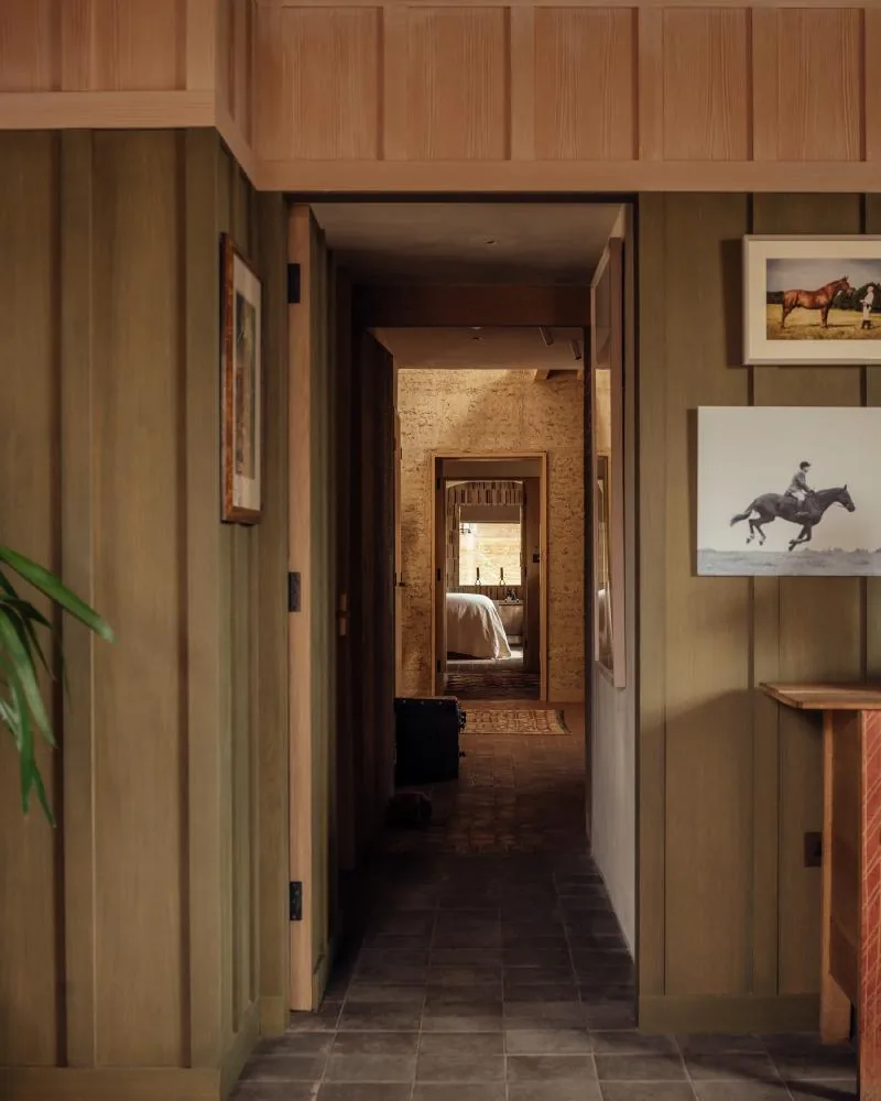 A green-panelled corridor leading toward a bedroom and an earth wall beyond.